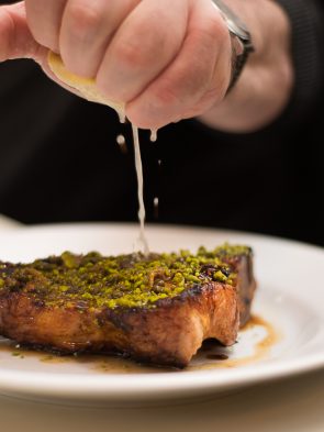 Chef squeezes lemon over steak plated at Guy's Restaurant, one of the most famous restaurants Merchant City Glasgow.